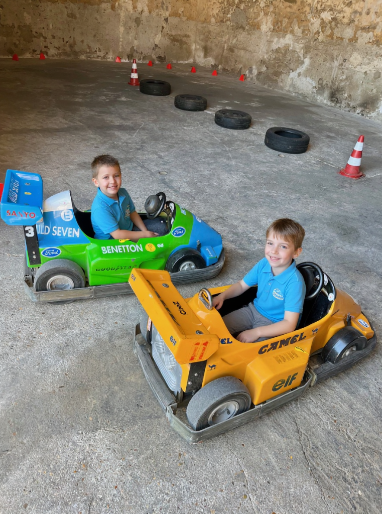 Deux jeunes enfants souriants dans des mini-karts électriques sur le circuit intérieur de la Ferme de La Forêt en Essonne.
