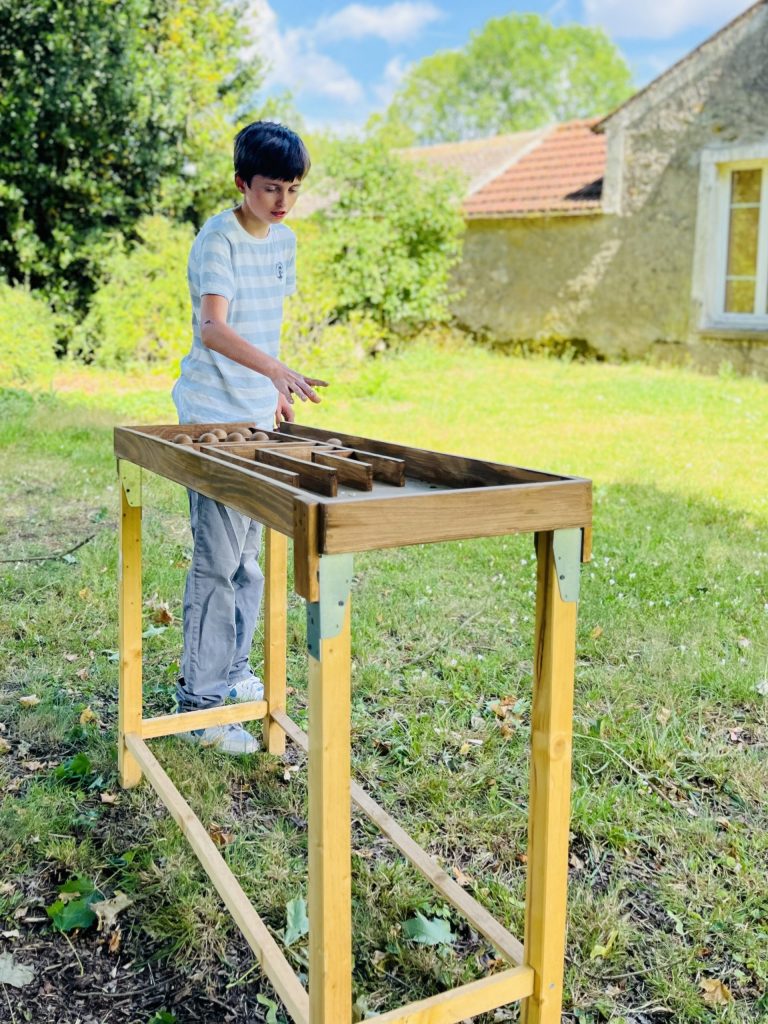 Un enfant s'amuse avec un grand jeu en bois dans le jardin de la Ferme de La Forêt, une ferme de loisirs située en Essonne.
